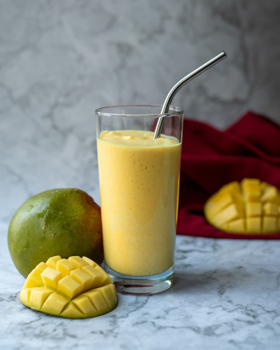 Mango milk shake beside a cut mango