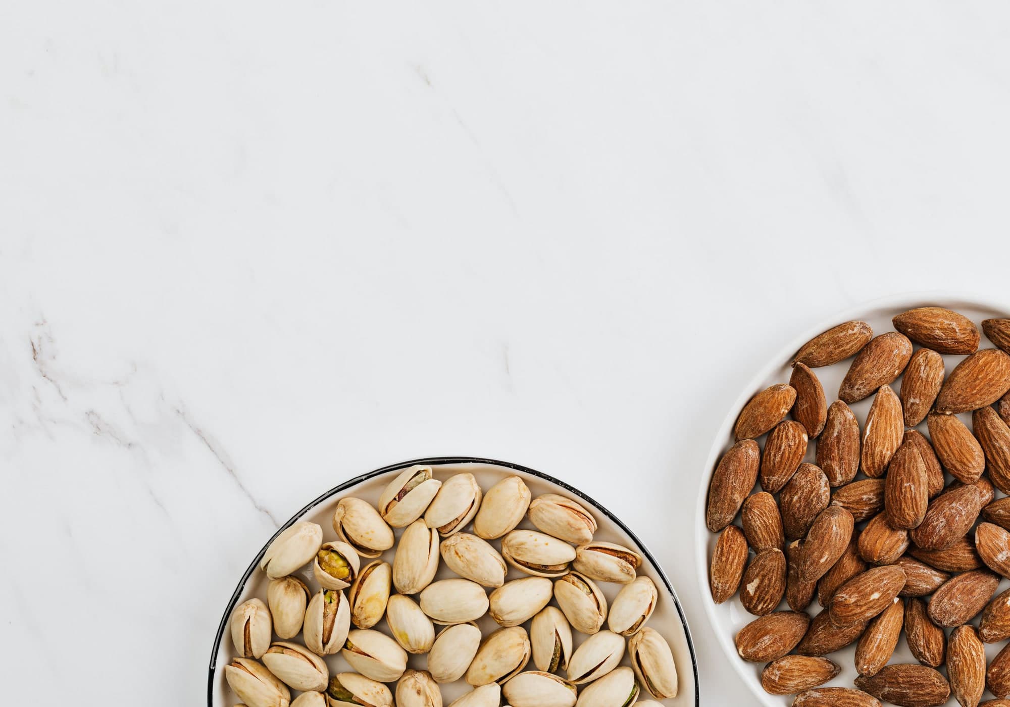 Pistachios and almonds in bowls on white marble
